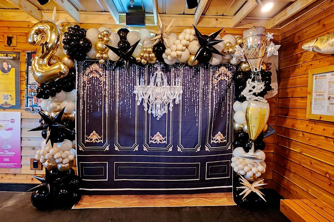 Black, ivory and gold balloon installation framing an ornate chandelier backdrop
