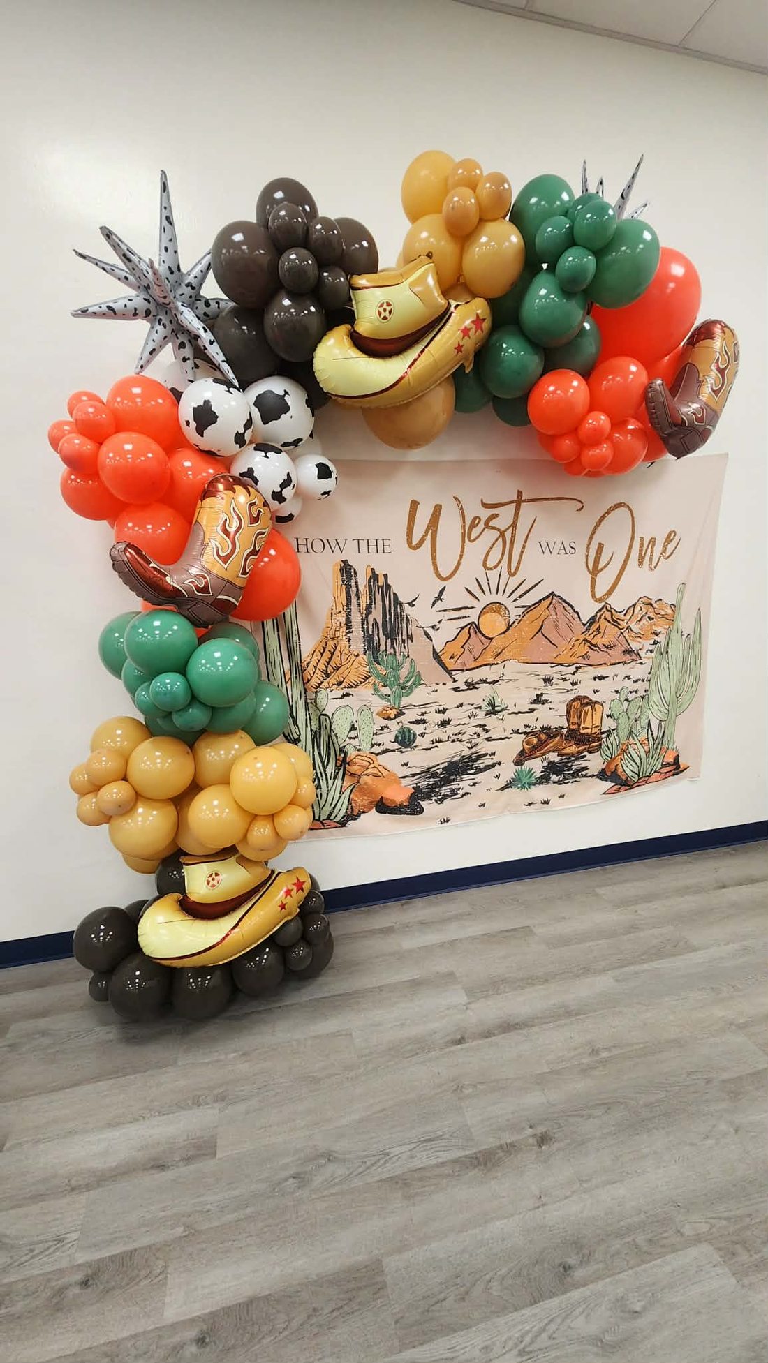 Western-themed balloon arch in terracotta, sage and mustard framing a desert backdrop