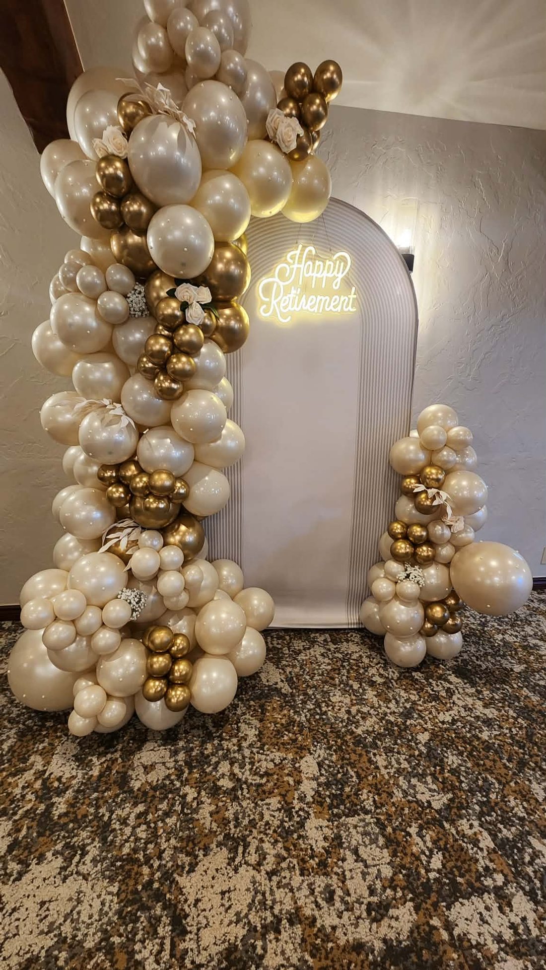 Champagne, ivory and gold balloon installation beside an arched backdrop with a neon sign