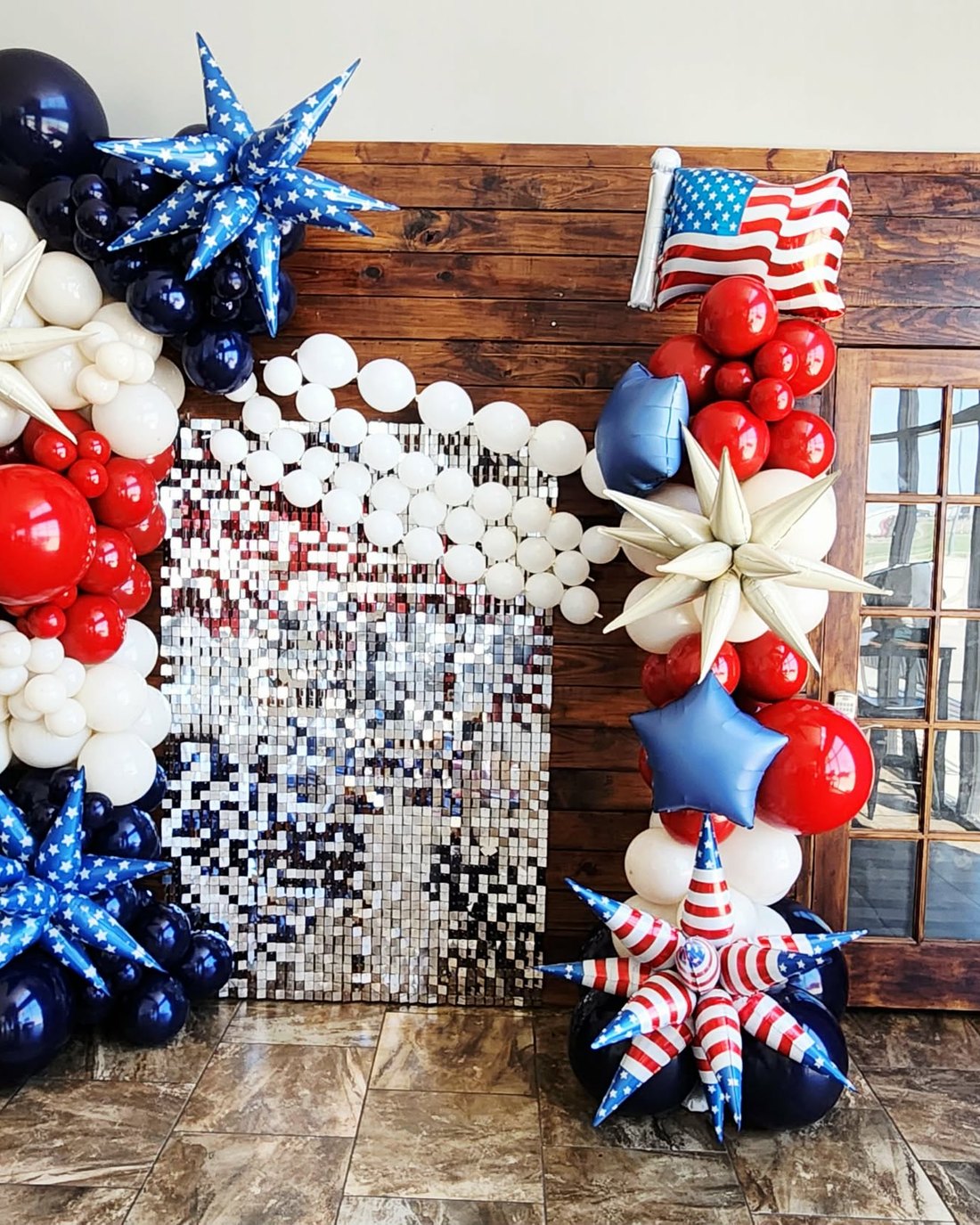 Wide view of a patriotic balloon and sequin backdrop with red, white and navy garlands and star-spangled foil bursts