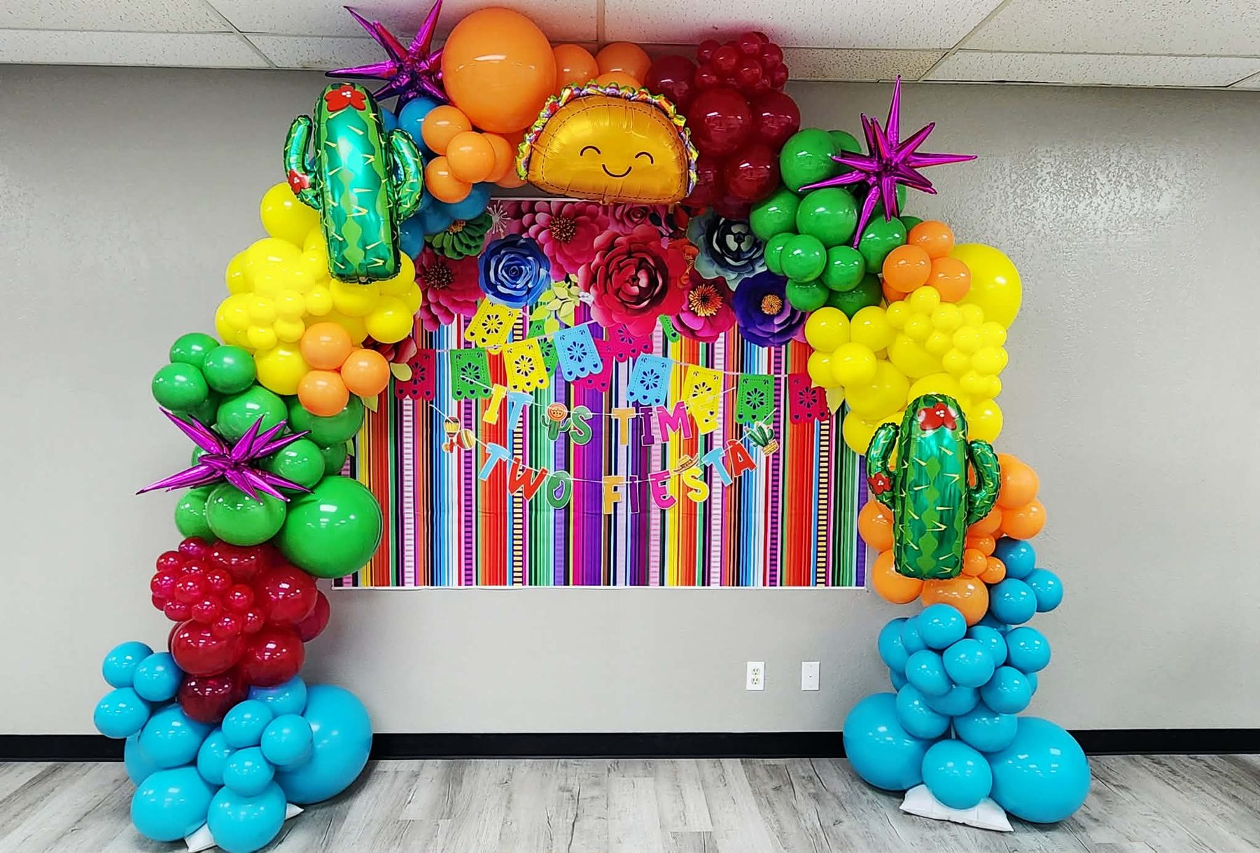 Vibrant fiesta-themed balloon arch with cactus accents over a serape backdrop